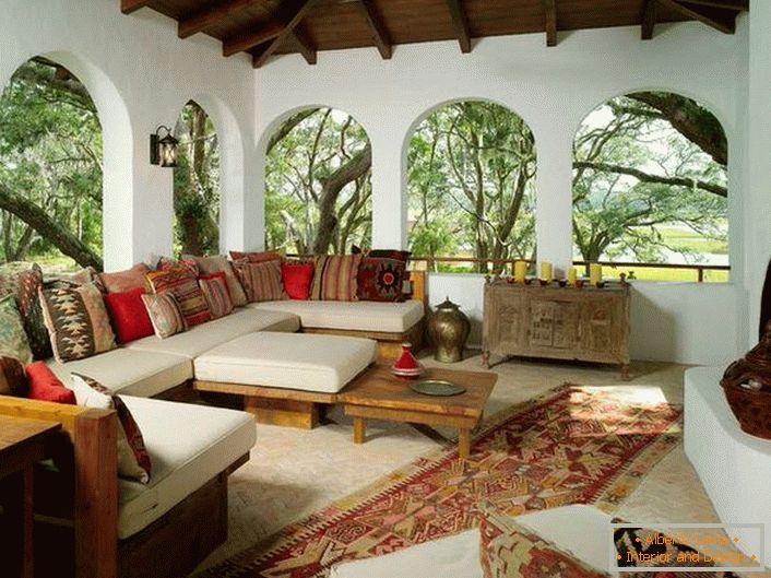 La véranda de la maison de campagne est décorée dans le style méditerranéen. Une caractéristique intéressante est le décor avec beaucoup de coussins colorés.