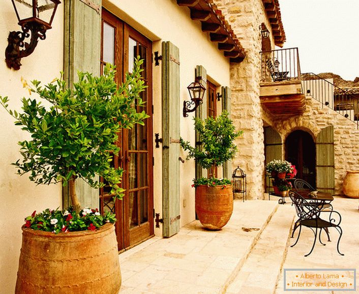 Le patio в средиземноморском стиле украшают горшки с живыми растениями. Привлекательный дизайн, мебель с витиеватыми спинками, керамические горшки создают уютную, расслабляющую атмосферу. 