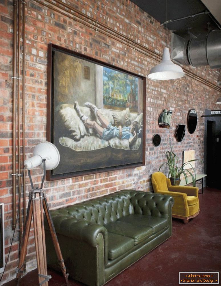 Grande peinture à l'huile sur le mur de briques d'un appartement de style industriel avec canapé rétro et fauteuil