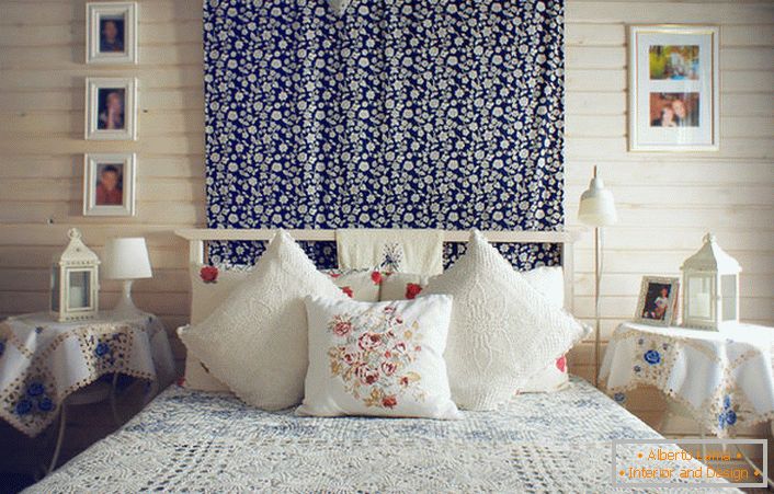 Conformément au style rustique, le lit est décoré d'un certain nombre d'oreillers avec des broderies rouges contrastantes. Les tables de chevet sont recouvertes d'une nappe à fleurs bleues délicates.
