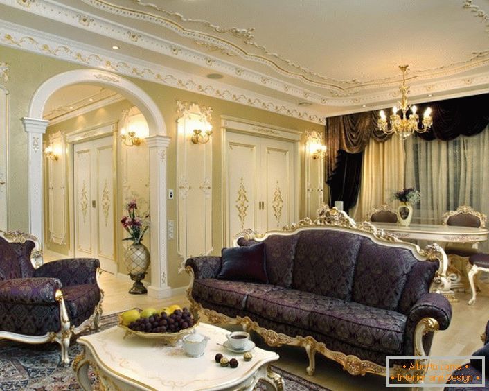 Un exemple d'une combinaison compétente de couleurs dans la décoration dans le style baroque. Les meubles d'ameublement, les lambrequins et les tapis, de couleur lilas, sont combinés avec les raisins sur la table et les fleurs. Intention de conception mince.