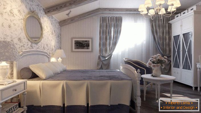 La chambre dans le style campagnard est faite dans des tons bleus. Le mur à la tête du lit est recouvert de papier peint à motif floral.