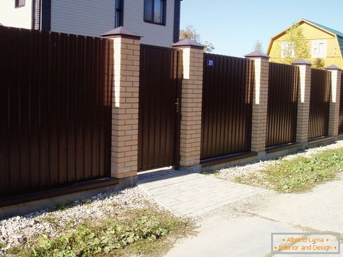 La clôture modulaire est brun foncé avec une finition en brique - un classique du genre, si l'on parle de la conception des zones suburbaines.