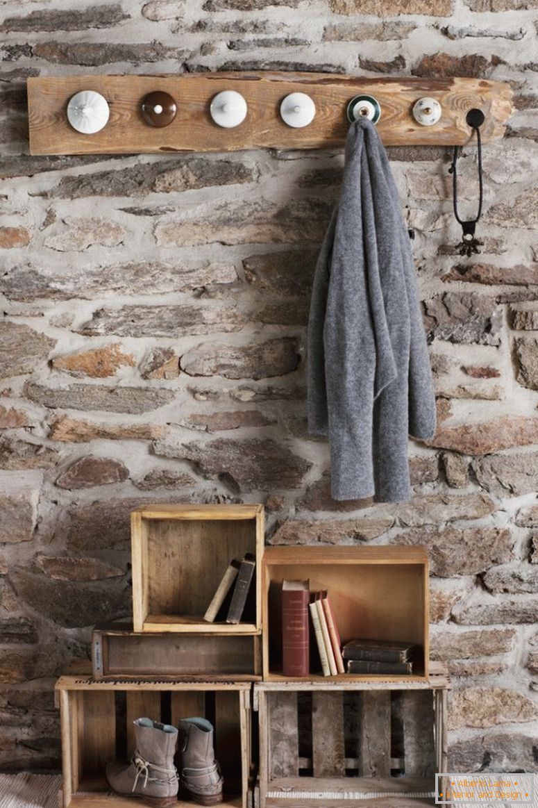 Vestiaire rustique en bricolage dans la chambre avec mur de pierre; patères faites de vieux couvercles en porcelaine et de vieilles caisses en bois sur le sol