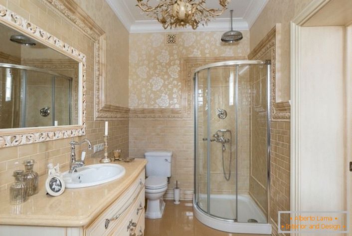 La salle de bain est décorée dans un style néoclassique. Un grand miroir, encadré par un large cadre, rend l'image complète.
