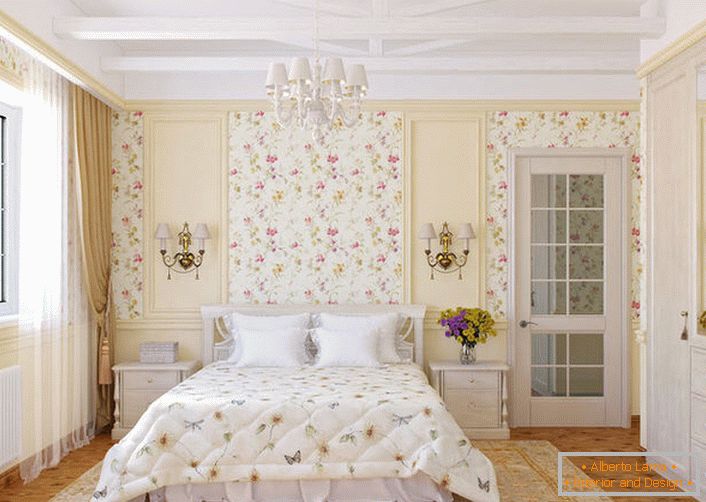 Les murs de la chambre dans le style campagnard sont décorés avec du papier peint à fleurs, qui se marient harmonieusement avec le couvre-lit sur le lit.