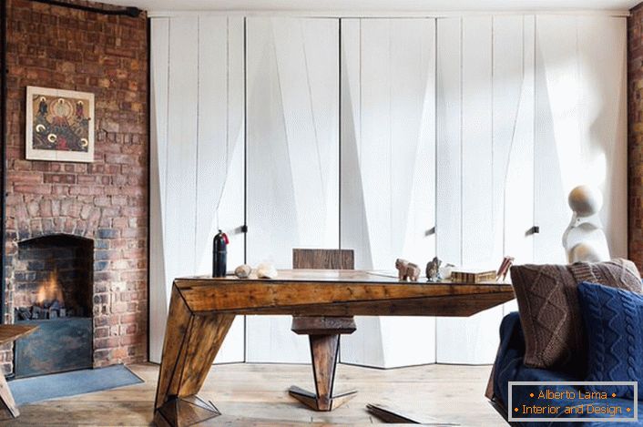 Le salon avec un bureau privé est décoré d'une cheminée à bois. Un élément décoratif inhabituel devient des oreillers à carreaux crochetés, ce qui rend le style loft chaleureux et confortable. 